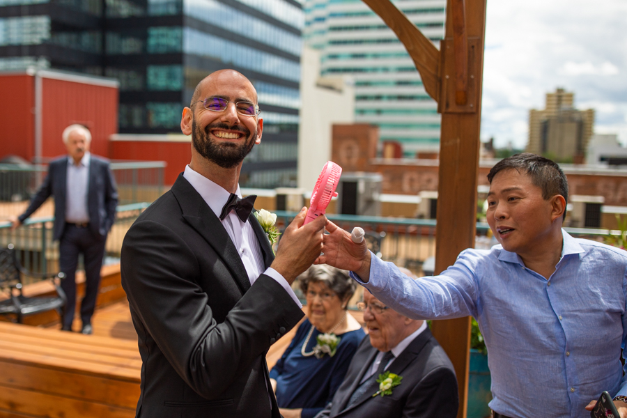 groom using a fan on rooftop elopement in edmonton